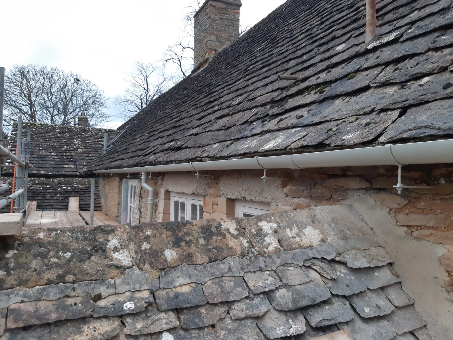Light grey half-round guttering along the eaves of a stone cottage with traditional roof tiles