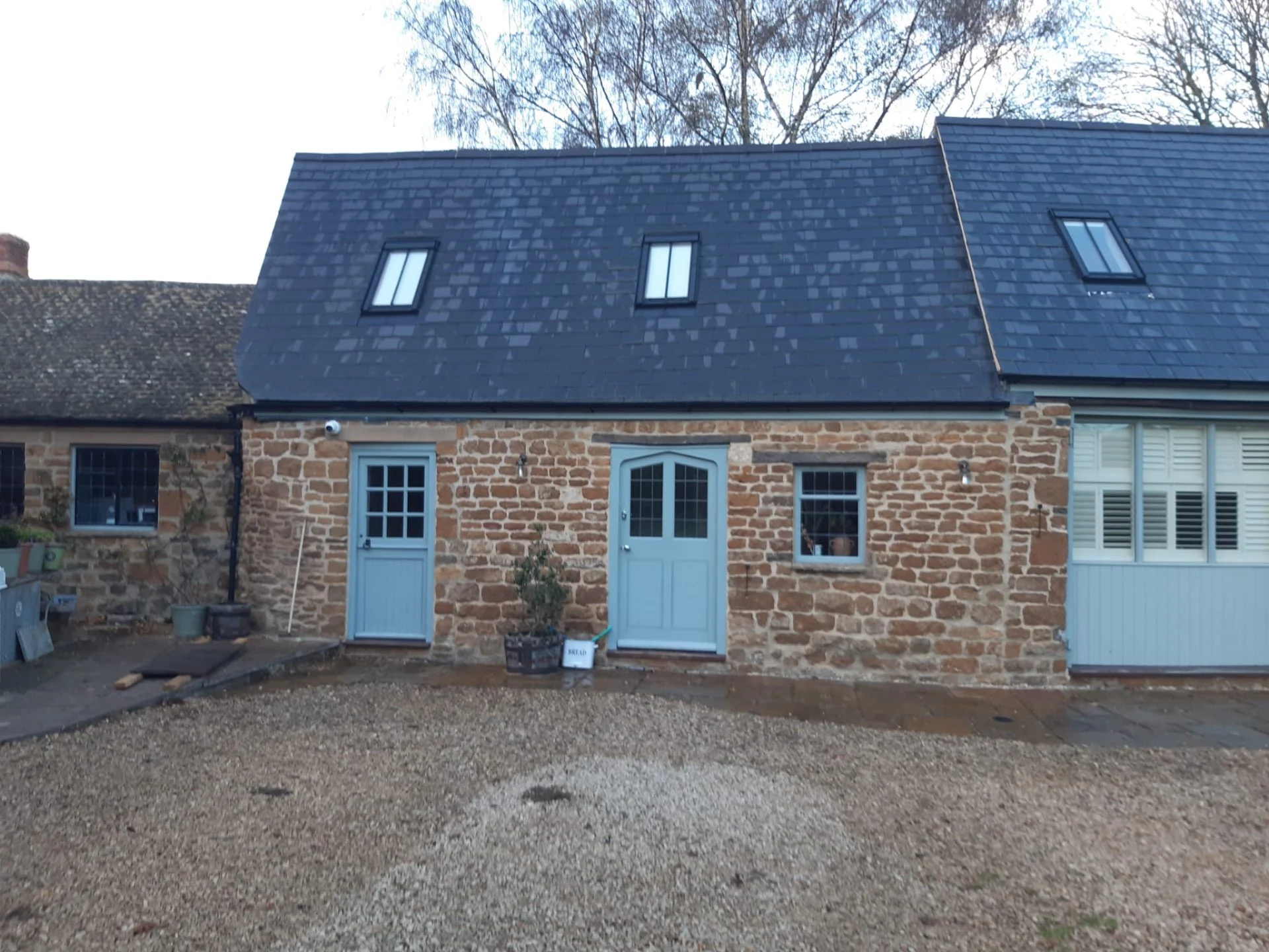 Dark guttering along a slate-roofed stone conversion with pale blue doors in the Cotswolds area