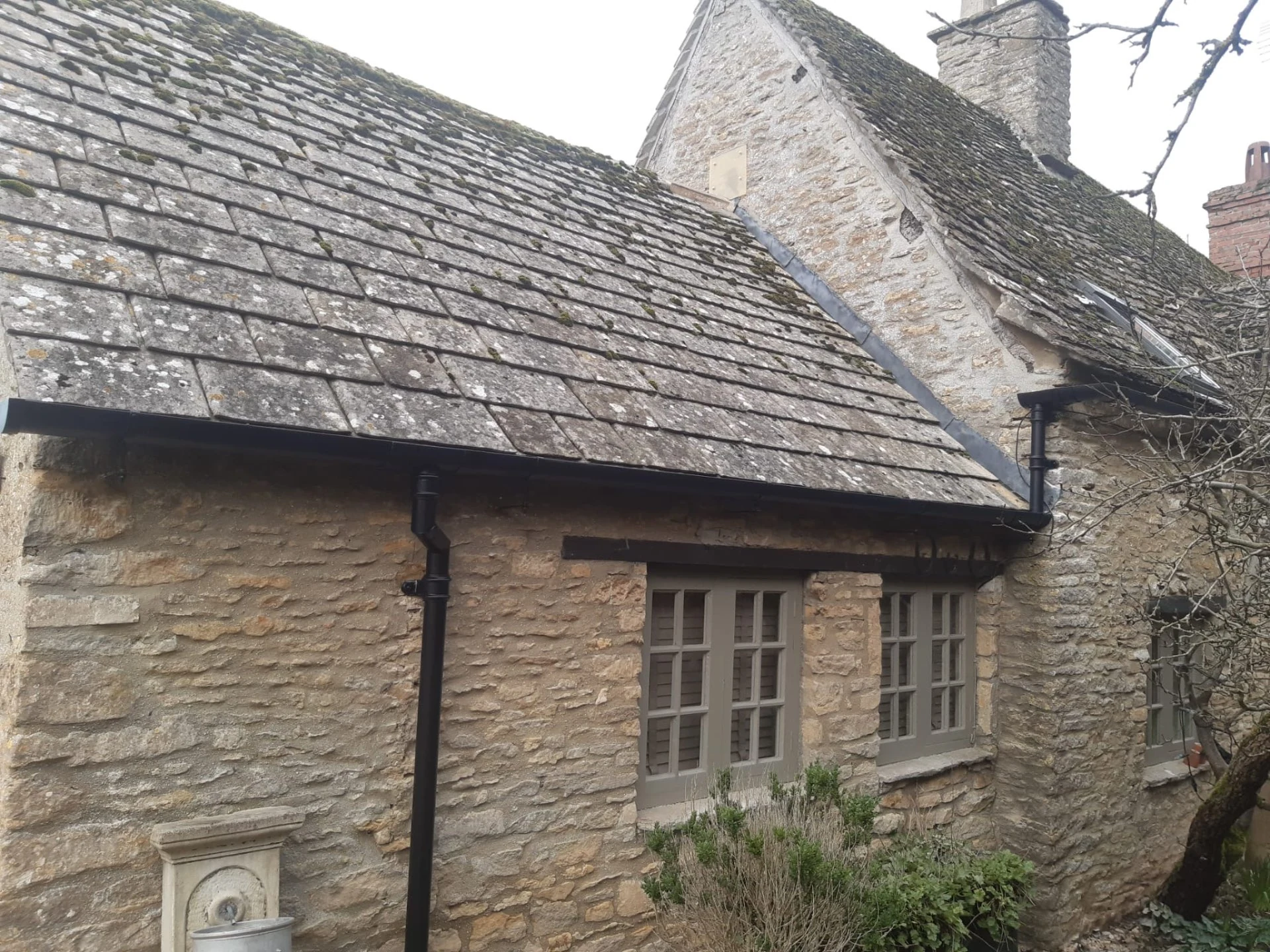 Dark gutters and downpipes at adjoining stone cottage roof sections